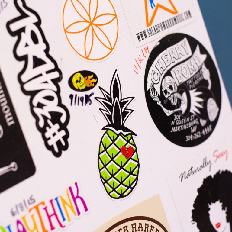 Colorful stickers featuring a green pineapple with a heart, along with various designs and logos, reflecting Hau Ink's custom printing services.