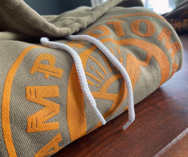 Hooded sweatshirt featuring bold orange graphic design and white drawstrings, displayed on a wooden surface, relevant to custom apparel offerings by Hau Ink.