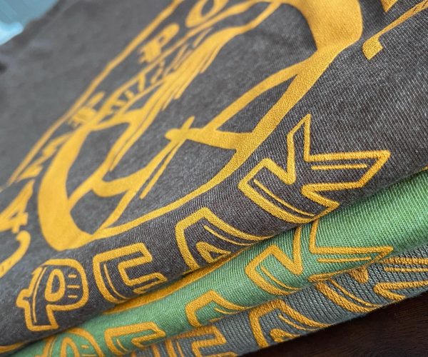 Stack of three colorful t-shirts featuring bold graphic designs in yellow and green, showcasing custom apparel options relevant to Hau Ink's merchandise offerings.